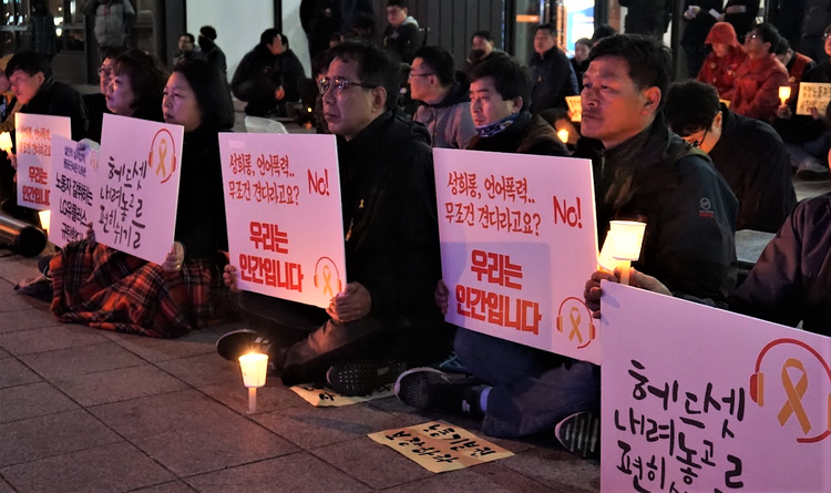 이미지 설명 : 촛불을 들고 집회 중인 사람들이 '헤드셋 내려놓고 편히 쉬기를', '성폭력 언어폭력, 무조건 견디라고요? NO! 우리는 인간입니다' 등의 구호가 적힌 피켓을 들고 있다.