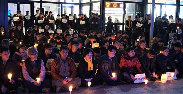 이미지 설명 : 촛불과 피켓을 든 사람들이 앉거나 서 있다.